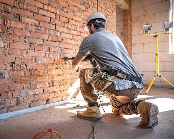 Persona trabajando en obra con casco, herramientas y reflectores a un lado.